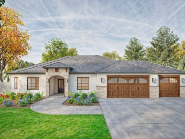 This image depicts a beautiful single-story home with a contemporary design. The house features a light-colored stucco exterior complemented by stone accents around the entryway and base of the walls. The roof has a dark gray shingle finish, and the three-car garage doors are made of wood with arched panels and decorative windows. The landscaping includes vibrant flower beds with colorful plants and neatly trimmed green grass. The curved concrete pathway leads to a covered front porch framed by a stone archway. The windows have dark trim, adding contrast and modern appeal to the overall design. In the background, tall trees and a blue sky complete the serene setting.